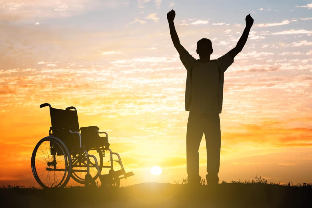 man standing with wheelchair behind him, celebrating