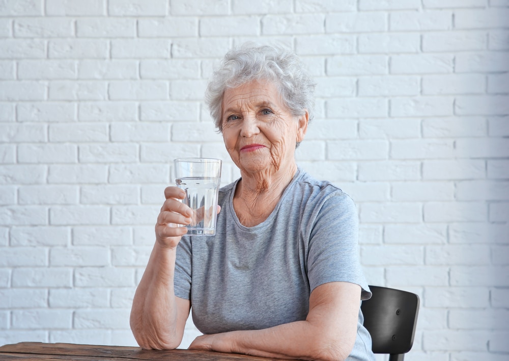 Elderly woman sitting and drinking a glass of water at table.