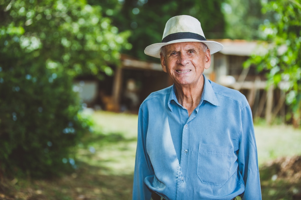 Elderly man at farm on a summer day wearing a hat for skin protection.