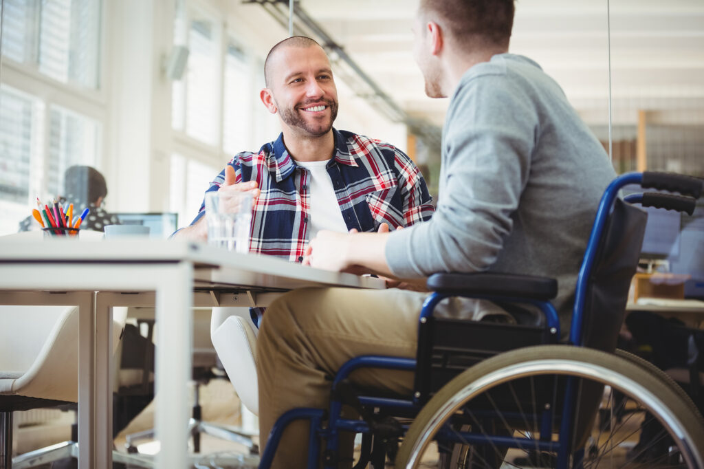 Working with people with disabilities. Handicap businessman discussing while sitting with colleague in creative office. 